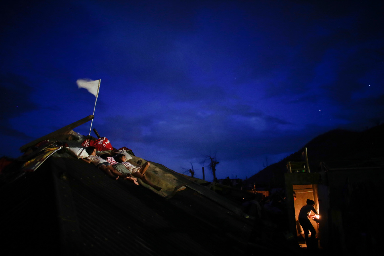  Children sleep on the collapsed roof of their house as their mother prepares dinner in Palo, Leyte   