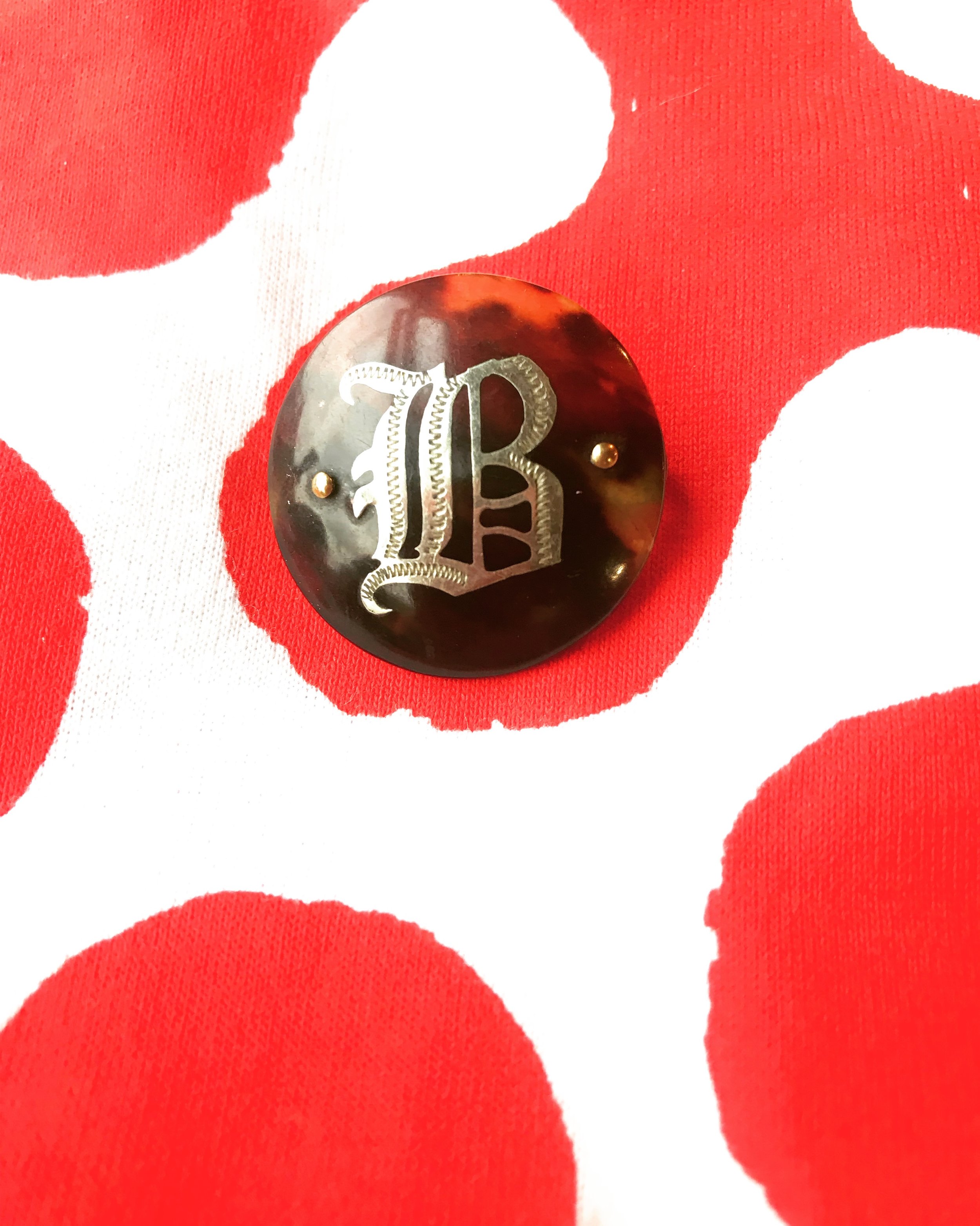 B is for bedlam. Silver on tortoiseshell button laid against our print inspired by the Leocorno (unicorn) team flag of the ancient palio horserace of Siena.