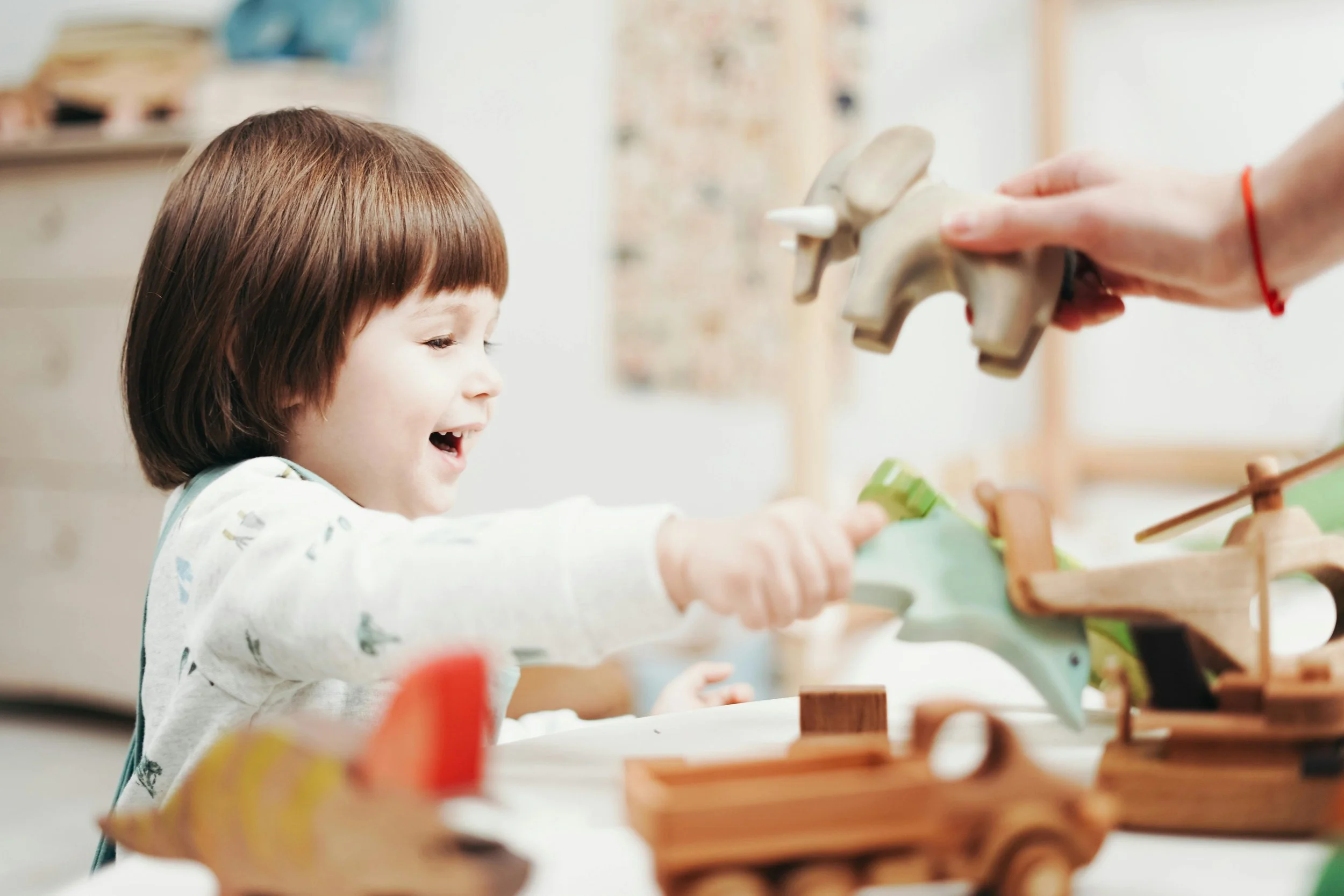 Young child playing with wooden toy animals at a table, smiling happily.
