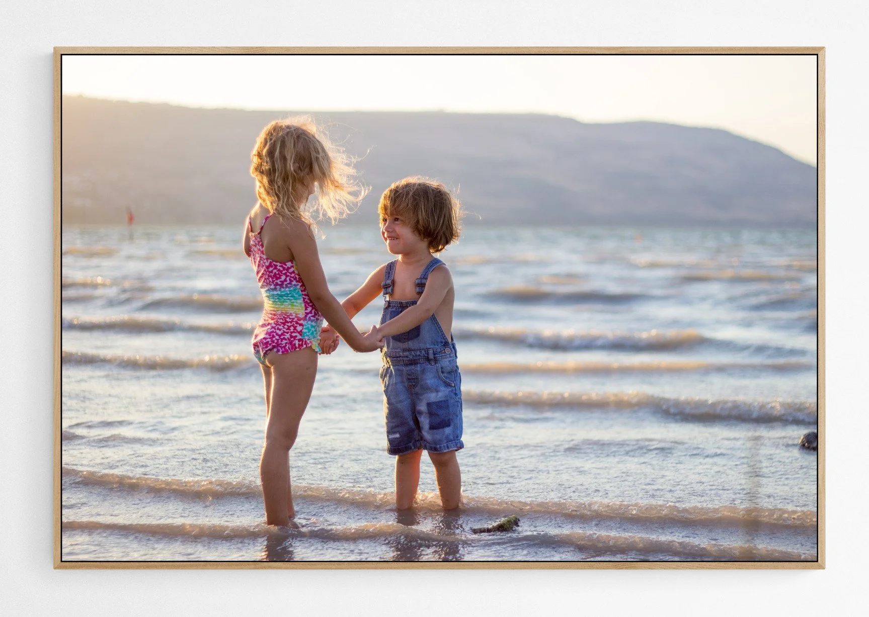 A high-quality, custom-framed fine art canvas print of children playing on the beach, showcased in a modern, light-filled home interior.
