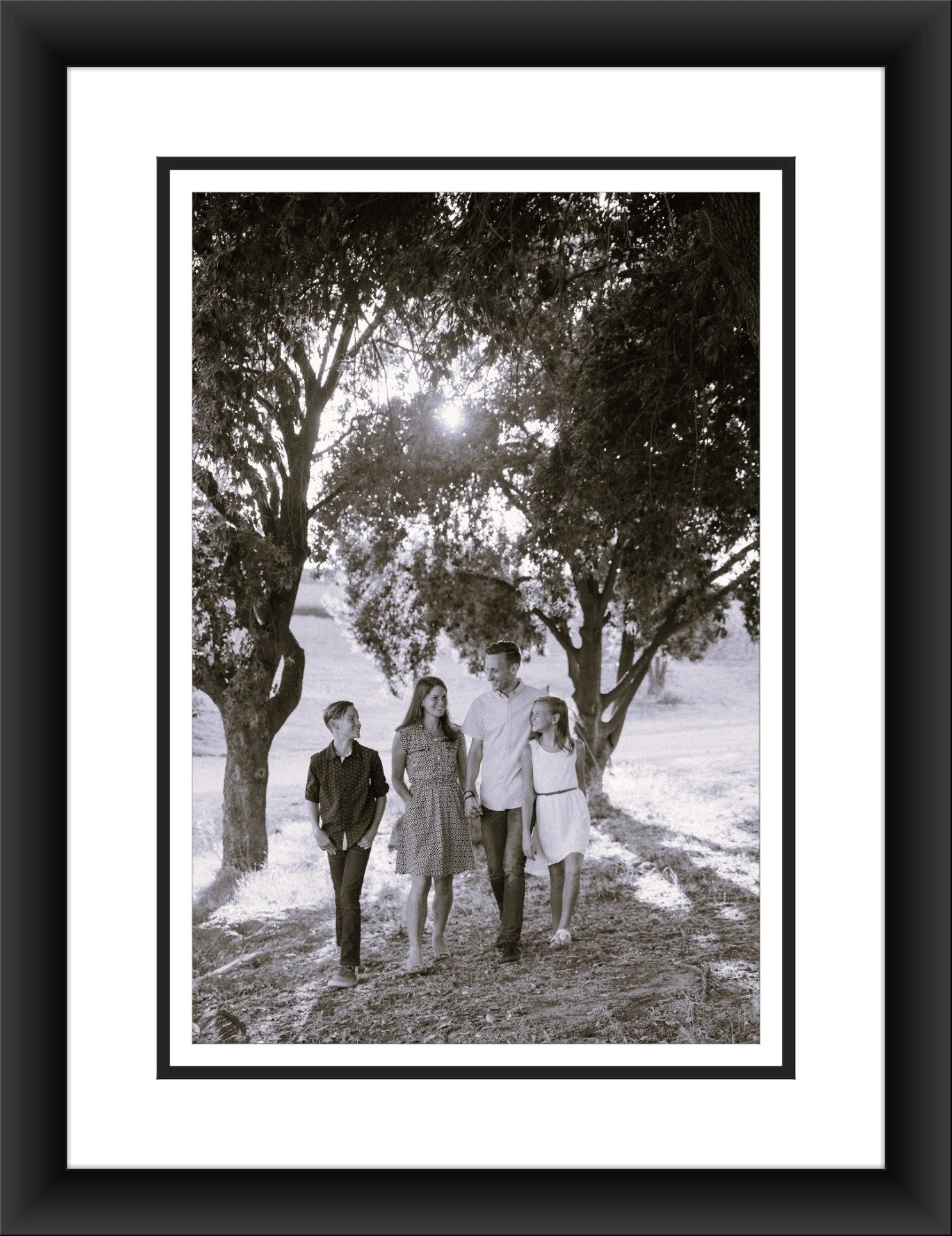 "A custom-framed black and white photograph of a family walking outdoors under trees, featuring a complementary black frame and a double mat with a black inner accent line."