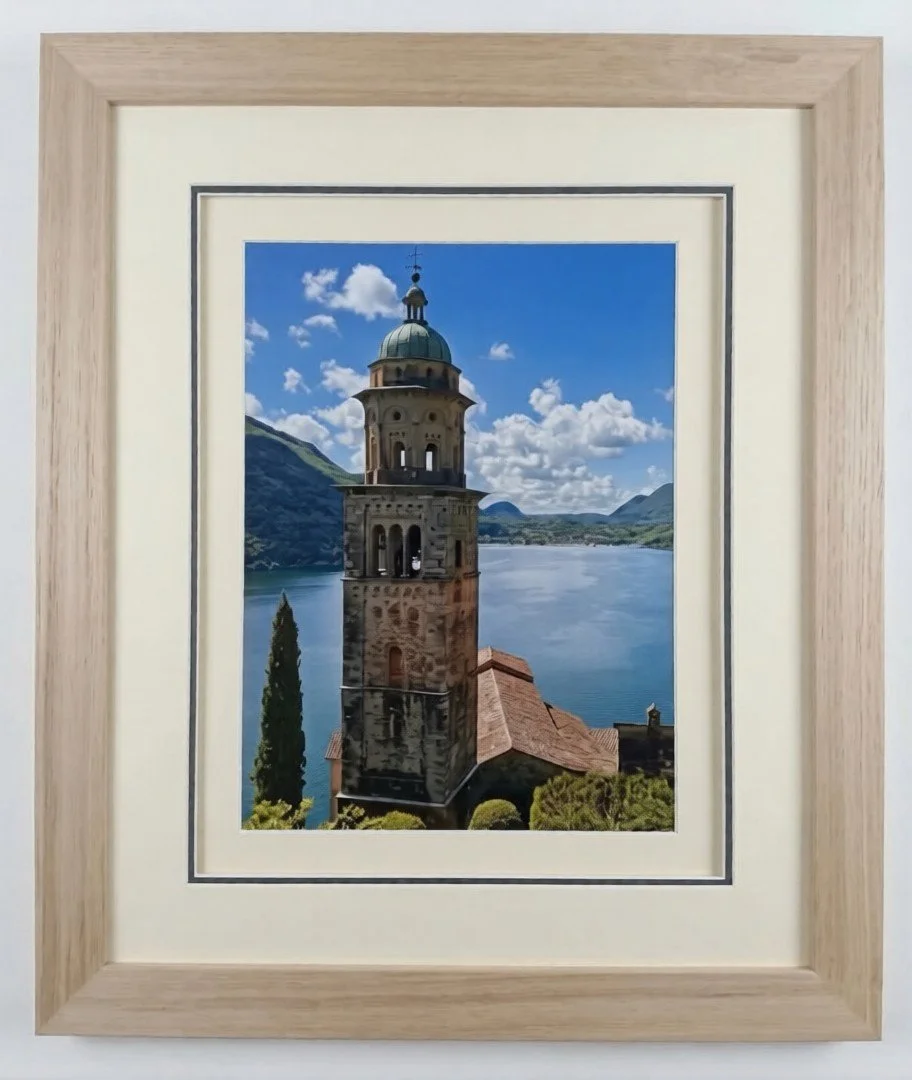 "A landscape photograph of a historic stone tower by a serene lake, professionally presented in a natural timber frame with a double mat."