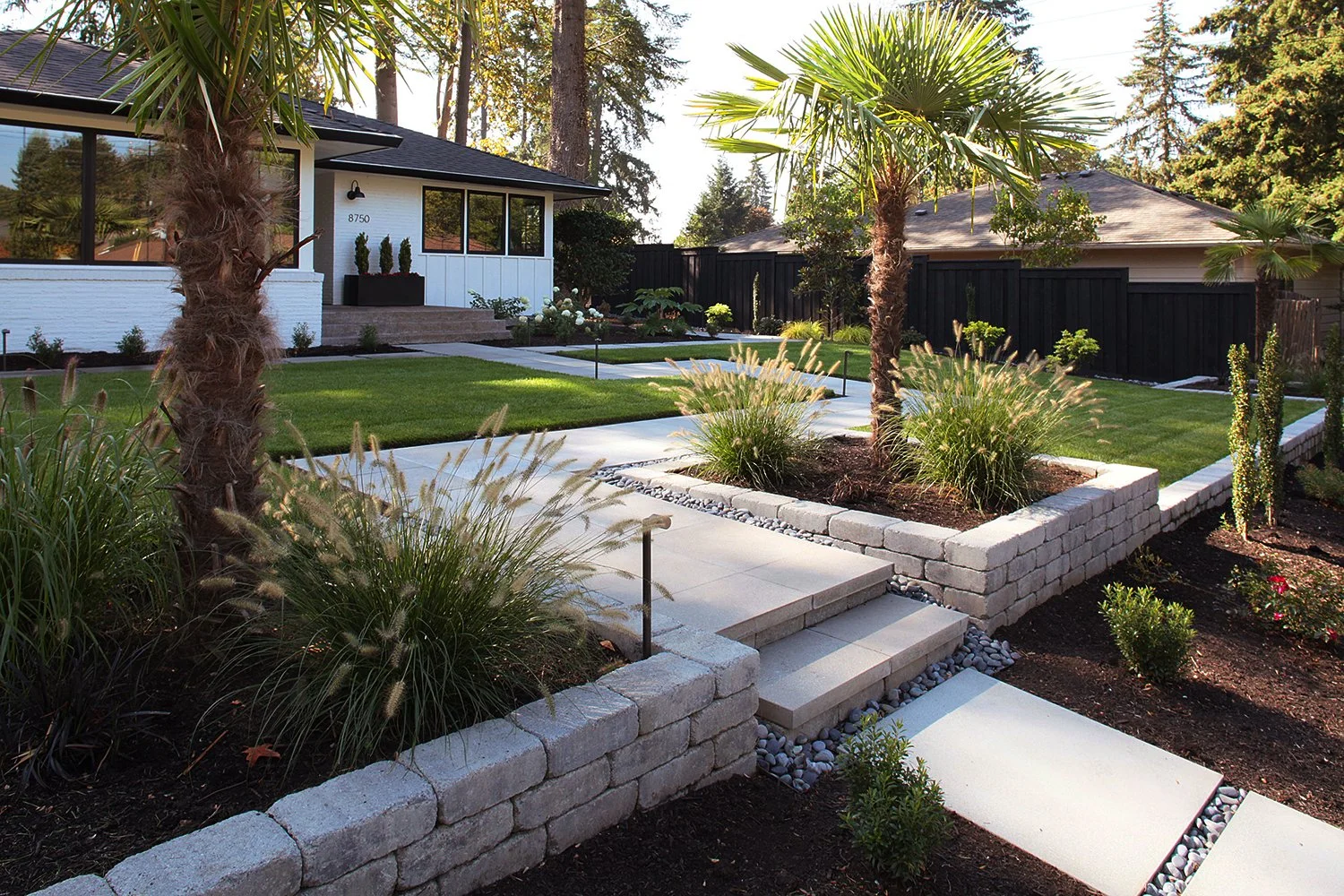 Raleigh Hills, Oregon contemporary landscape design. A zig zag paver walkway to the front door with black Mexican pebbles in between, paver retaining walls and planter boxes. 