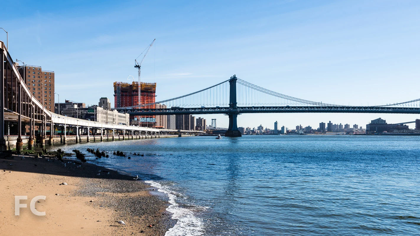 View from the East River Esplanade. Design of the exterior curtain wall of the tower includes two different wall types. At the north and south facades, panels are floor to ceiling glass with a bronze metal spandrel at the floor slab. For the east and west facades, flat glass panels are alternated with panels that tilt outward from the floor or the ceiling, adding dimension to the façade and a more dynamic reflection to the glass.