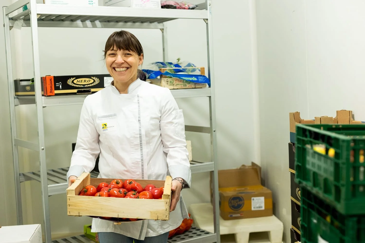 Portrait d'une collaboratrice dans la réserve de fruits et légumes avec une cagette de tomates dans les mains
