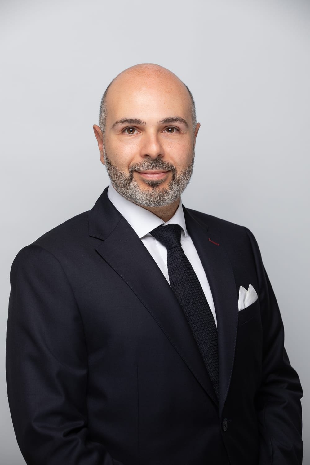 Portrait professionnel en studio d'un directeur en costume sombre et cravate noire, sur un fond gris clair.