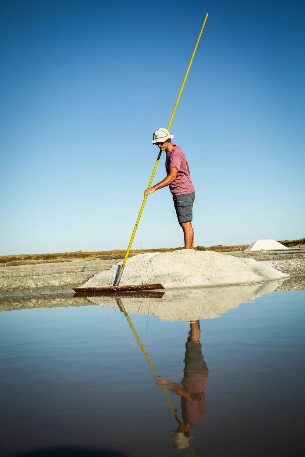 Paludier travaillant dans les marais salants de Guérande avec reflet dans l’eau