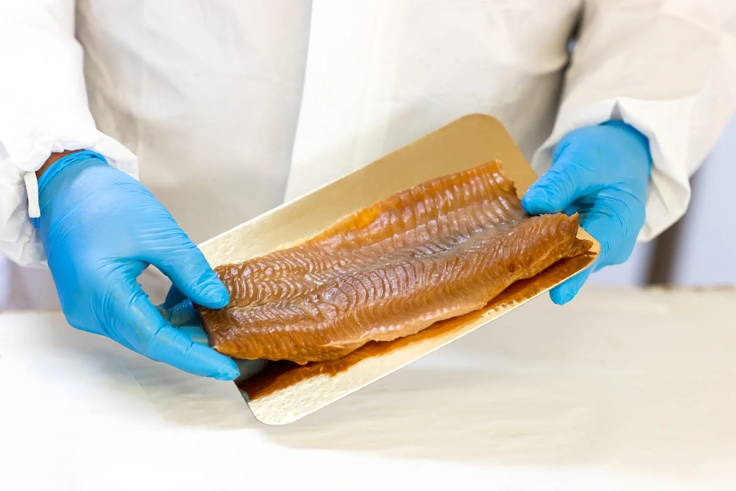 le producteur présente dans ses mains un filet de poisson fumé