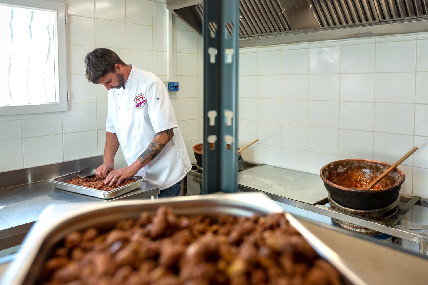 Gros plan sur des pralines caramélisées dans un récipient en inox, artisan en arrière-plan en train de trier les pralines