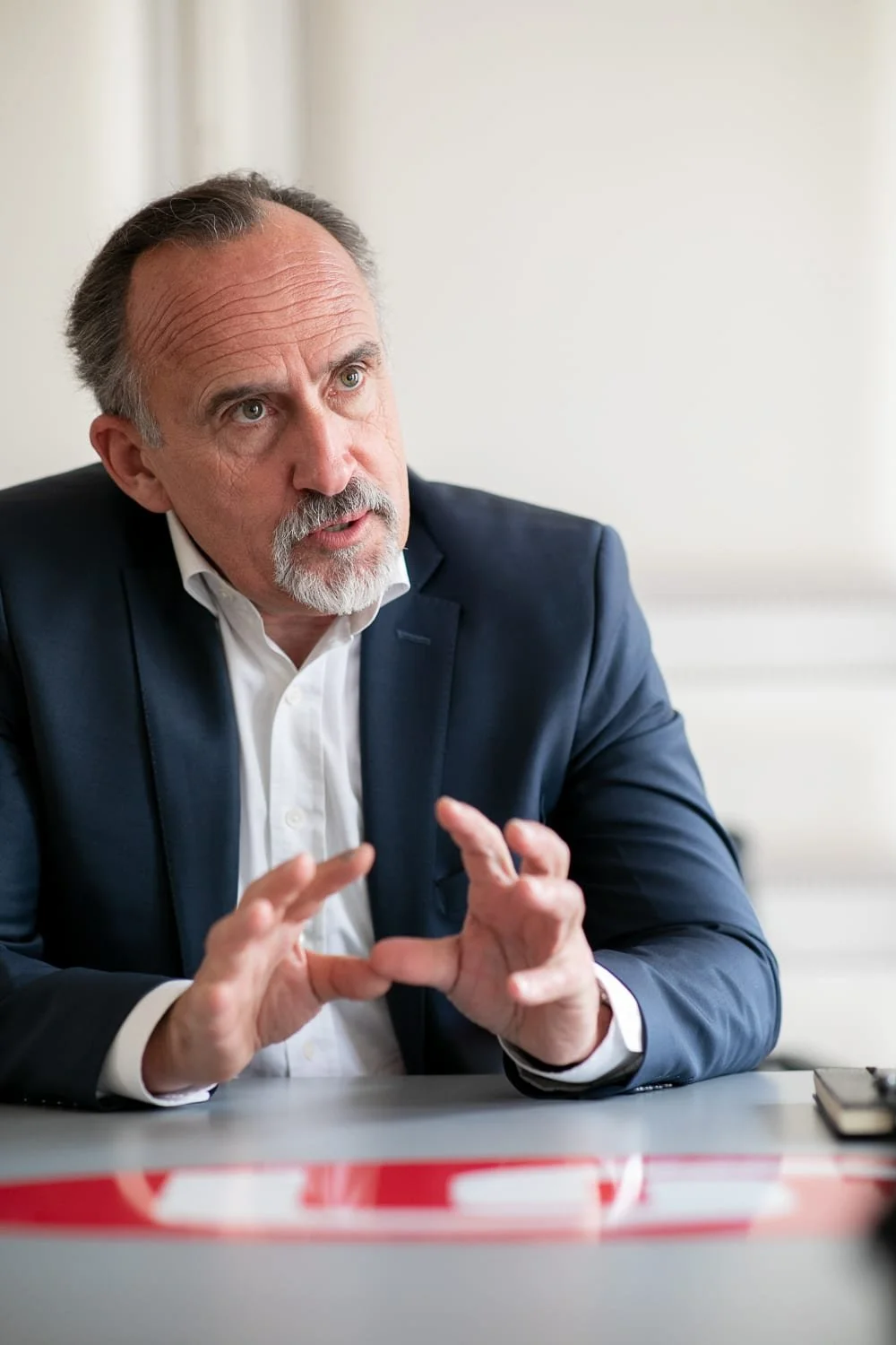 Portrait d'un dirigeant en situation d'interview, assis à une table et accompagnant ses propos de gestes des mains.