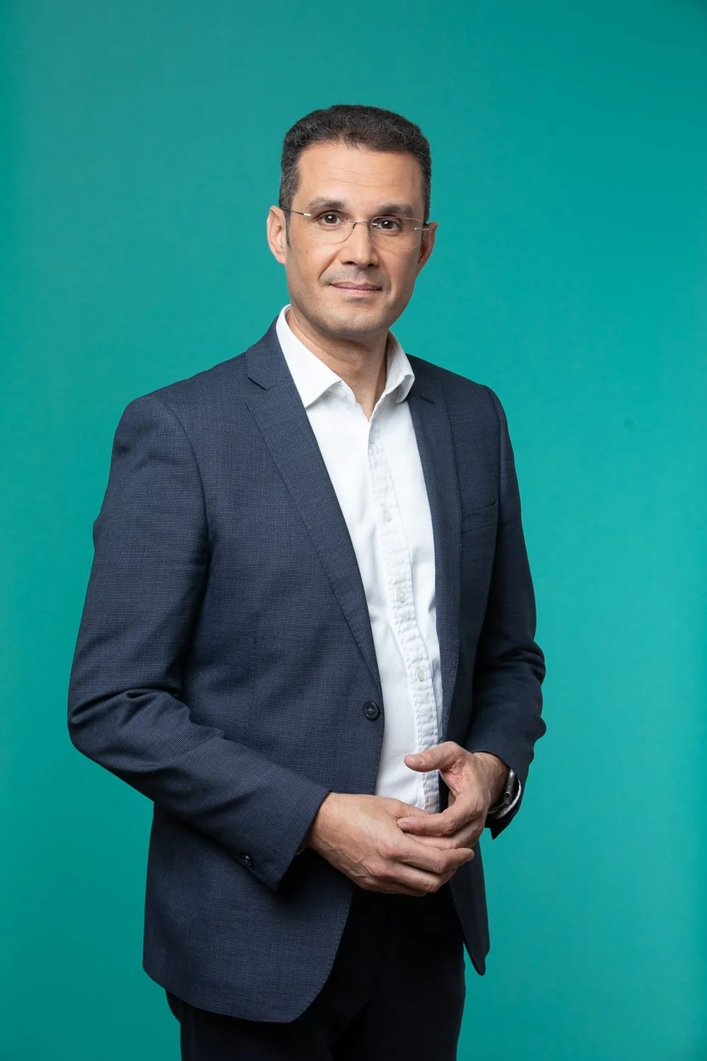 Portrait corporate en studio d'un homme en costume bleu et chemise blanche, debout devant un fond vert turquoise.