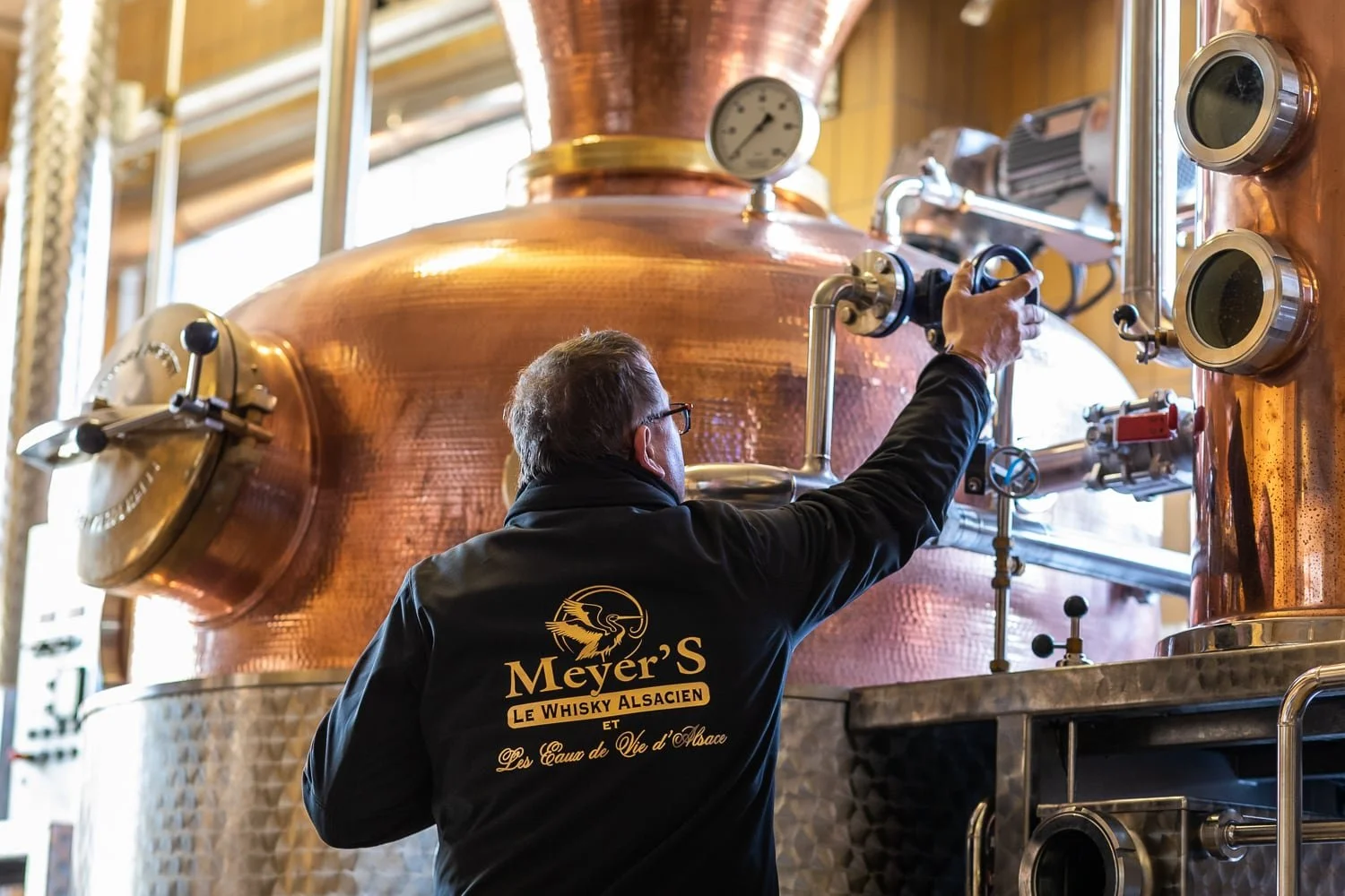 Artisan distillateur en situation devant  un alambic en cuivre dans une distillerie alsacienne