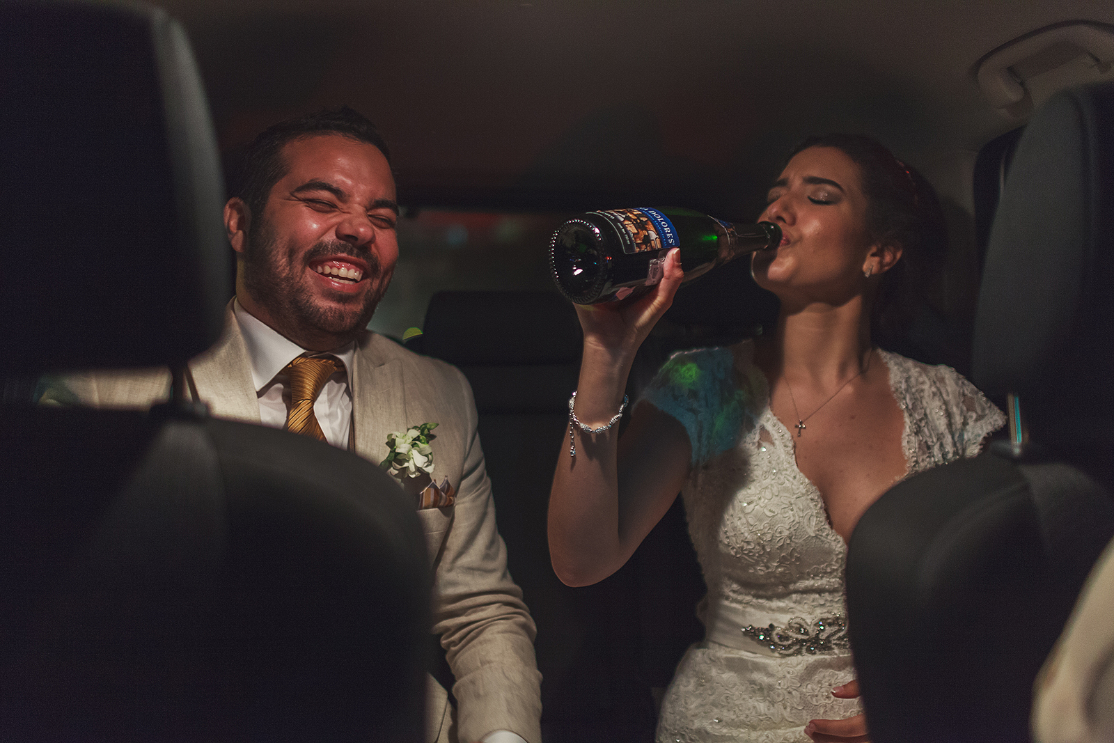 Novio ríe mientras novia bebe directo de la botella de champagne en el automóvil rumbo a la recepción de su boda en Grand Mayan Nuevo Vallarta