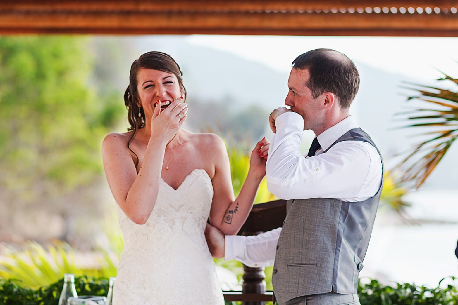 Bride laughs at groom after their first kiss while groom wipes lipstick off his lips