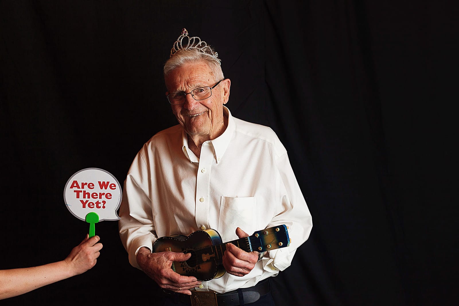 Bride's grandfather wears a tiara and hold a tiny guitar for the wedding photo booth