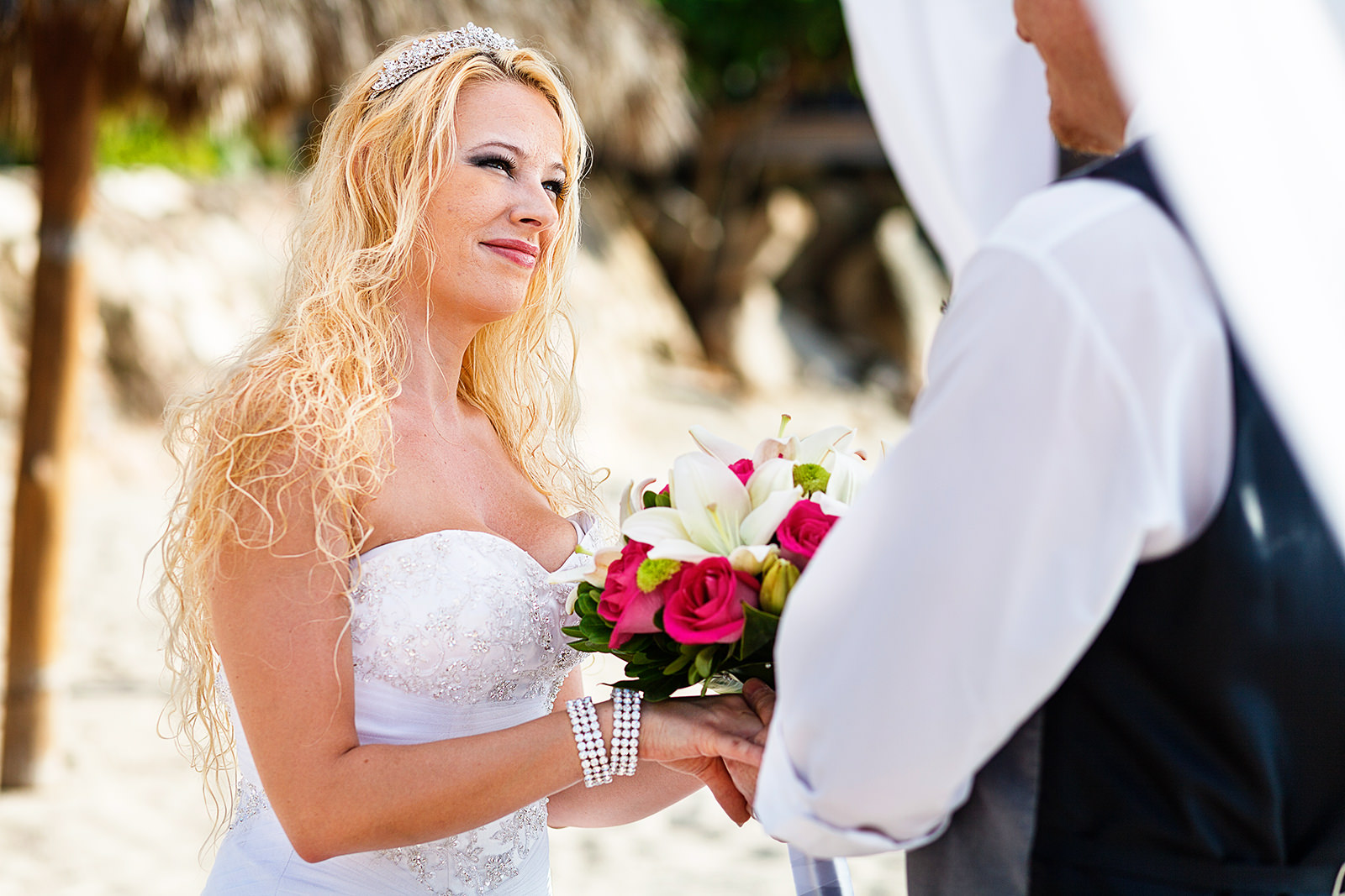 Bride with tiara looking at groom during ceremony on the beach