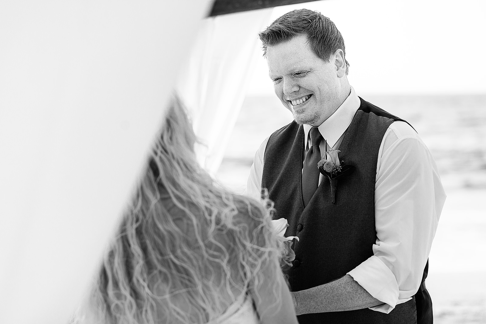 Groom smiling at bride during ceremony on the beach