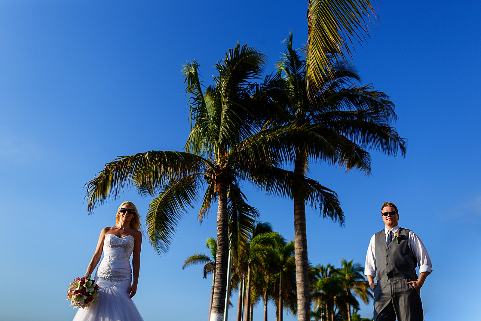 bride and groom portrait with palm trees between them and blue sky as background