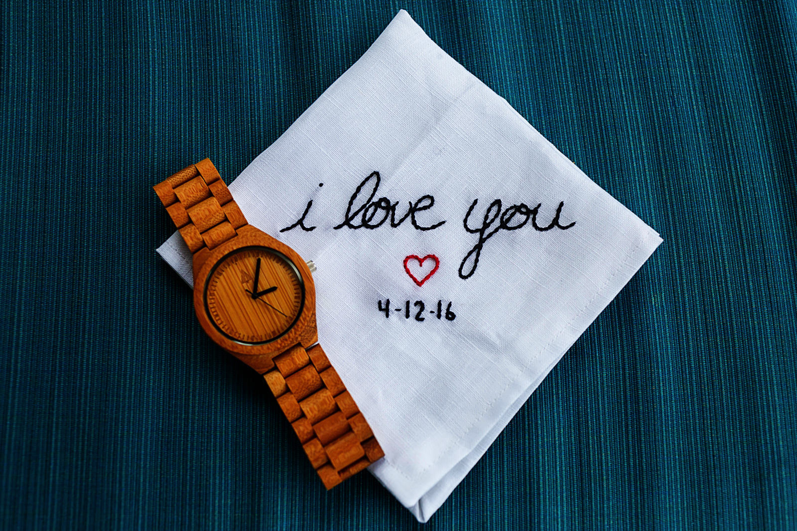handkerchief with words I LOVE YOU and wedding date embroiled next to wood wrist watch