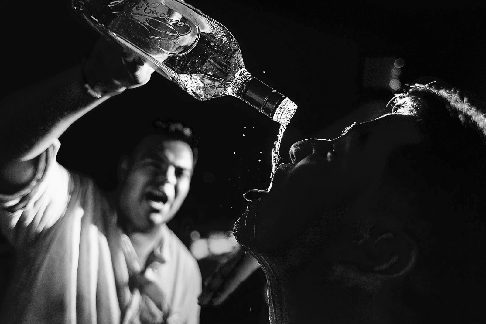 Groom pouring tequila straight from the bottle into a guest's mouth