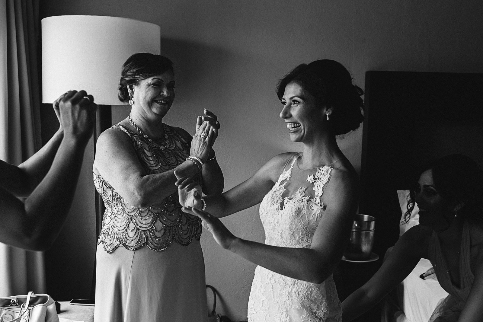 Bride and mother-of-the-bride laughing while bridesmaid help her with the wedding dress