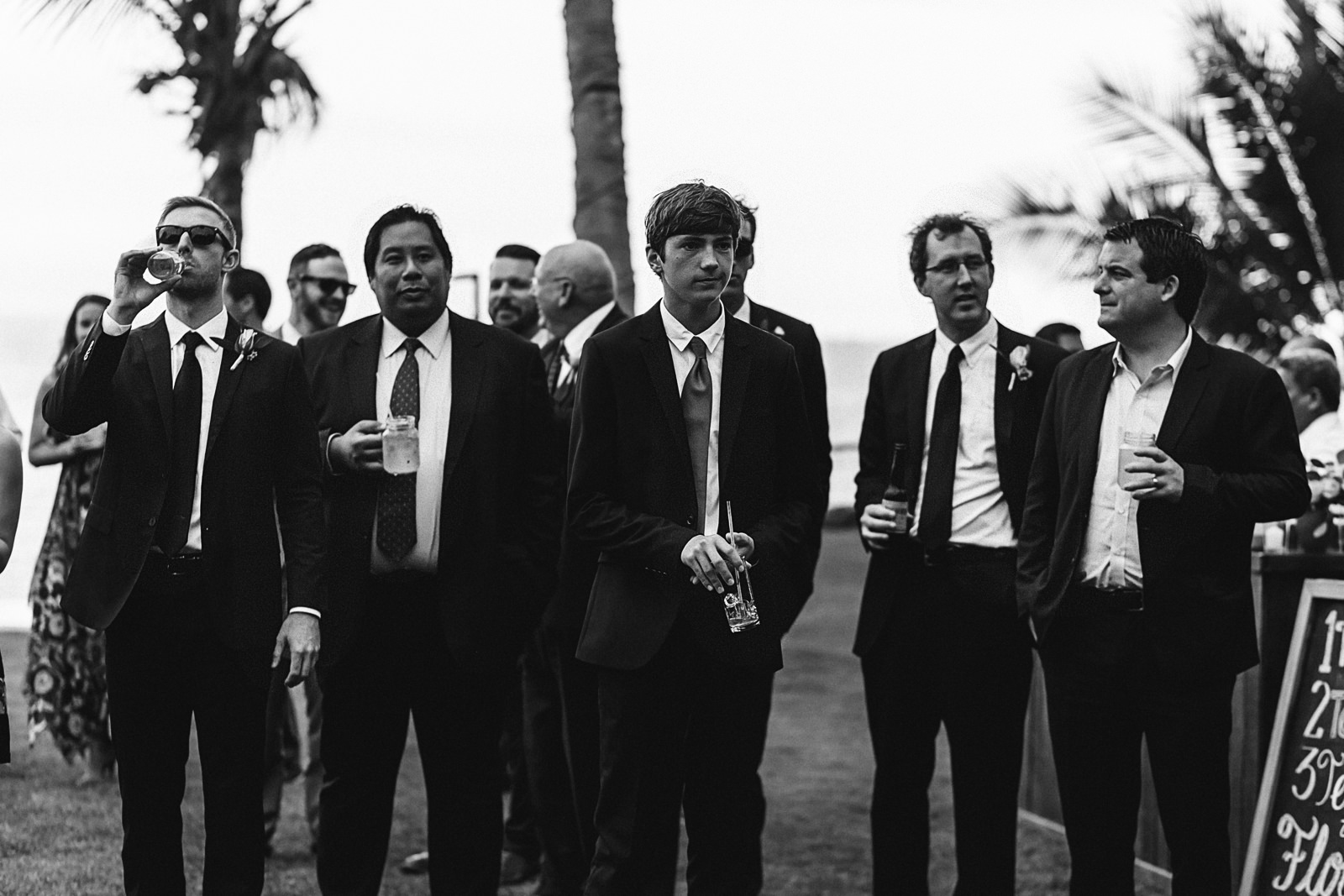 black and white photo of groomsmen in suit holding drinks at reception