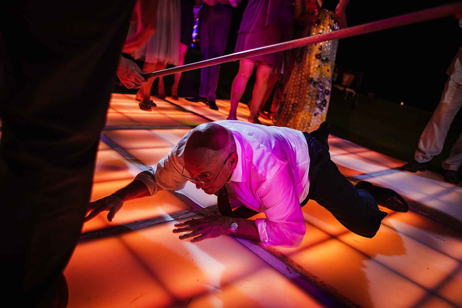 Father of the groom crawling under the limbo at wedding reception party