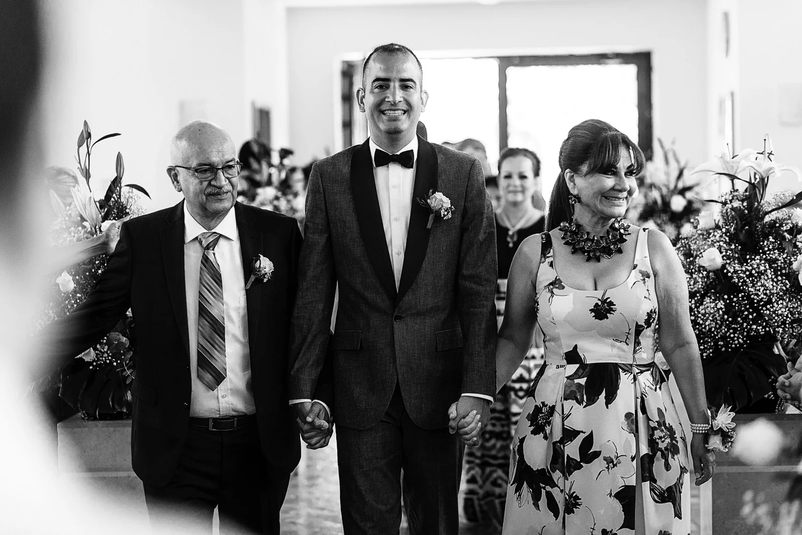 Novio y sus padres caminando hacia el altar para comenzar ceremonia religiosa de boda