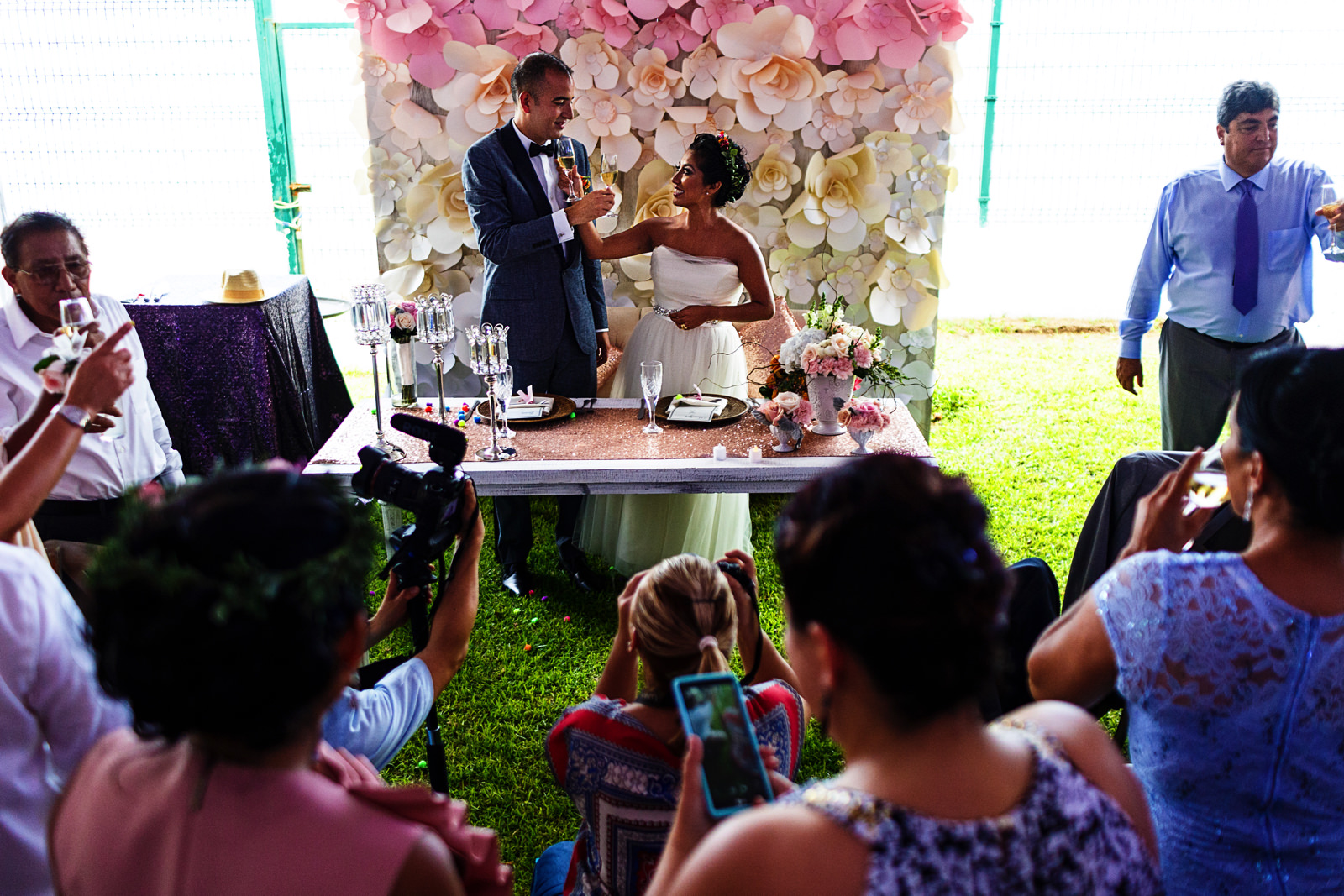 Novios cruzando copas de champagne entre una multitud de camaras e invitados