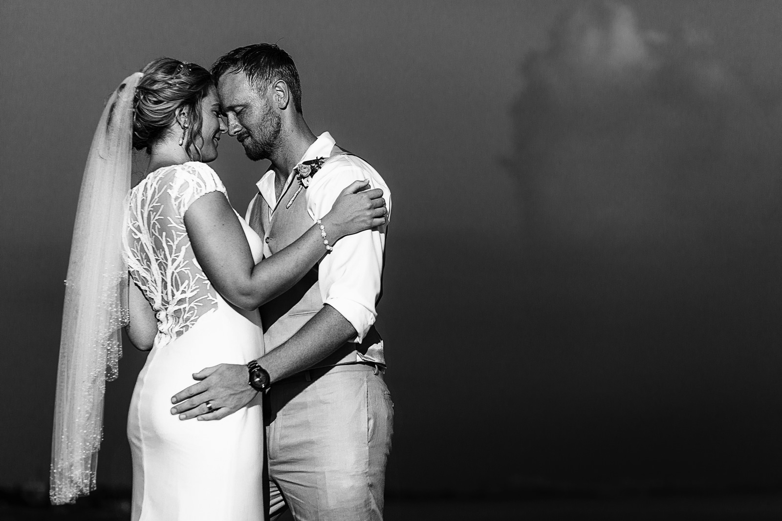 Black and white portrait of groom and bride standing face to face against the sky