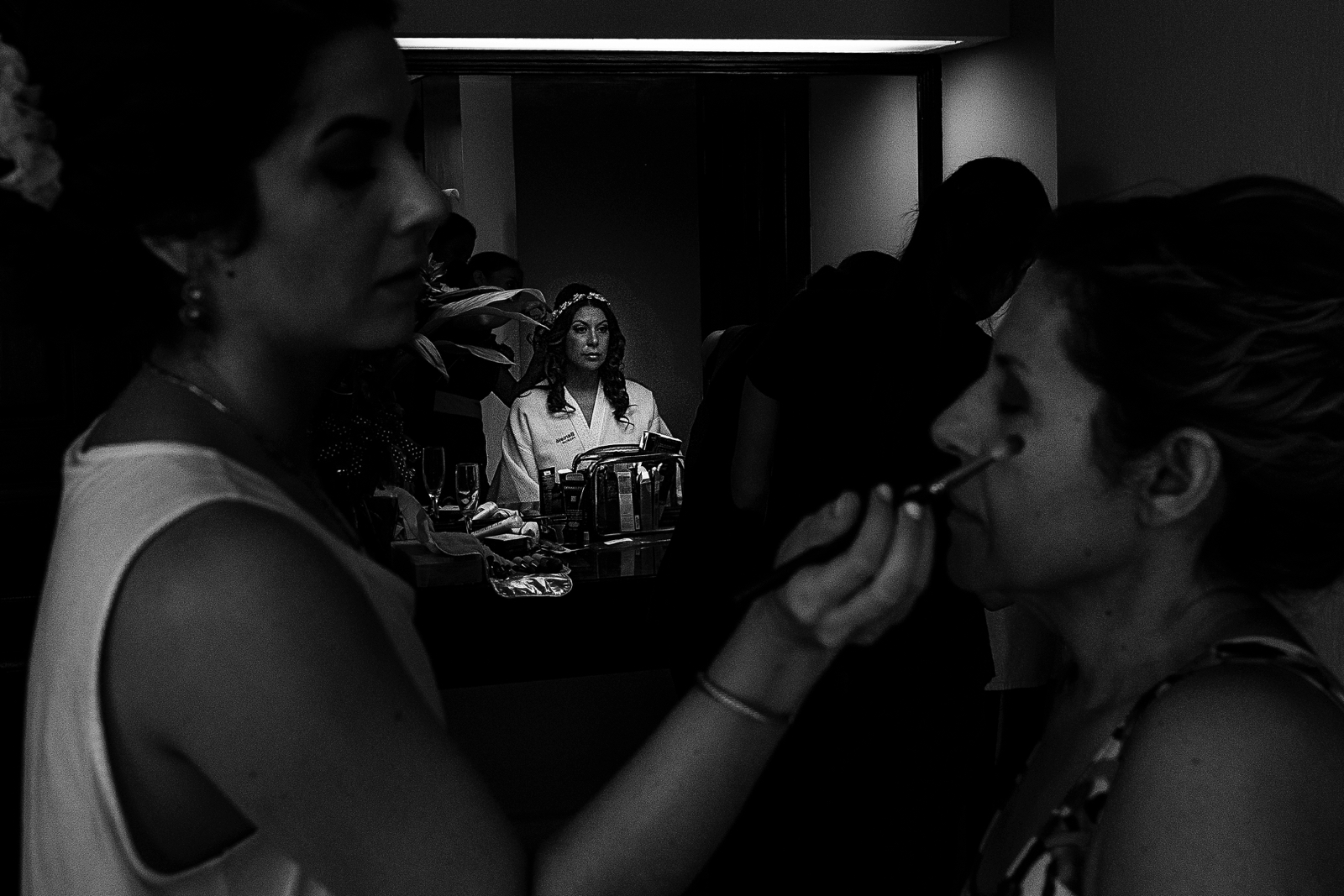 Bride having her make up done in front of the mirror while the sister does her mom make up
