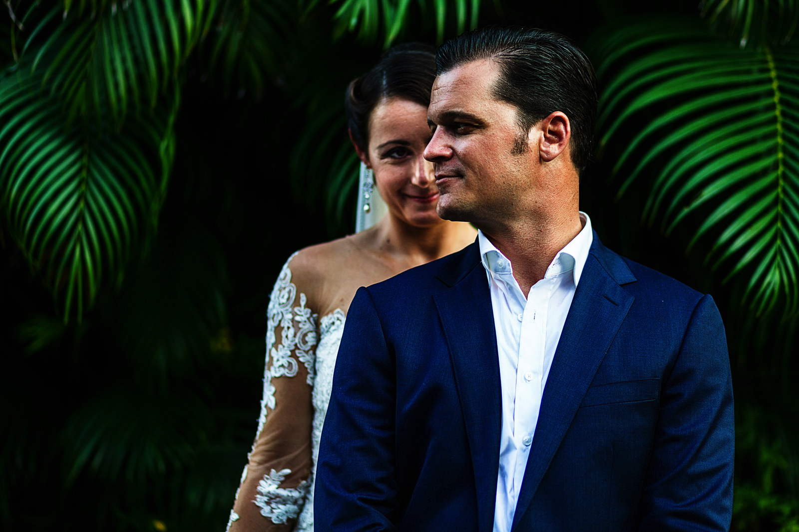 Portrait of the couple standing in front of palm leaves, bride behind the groom