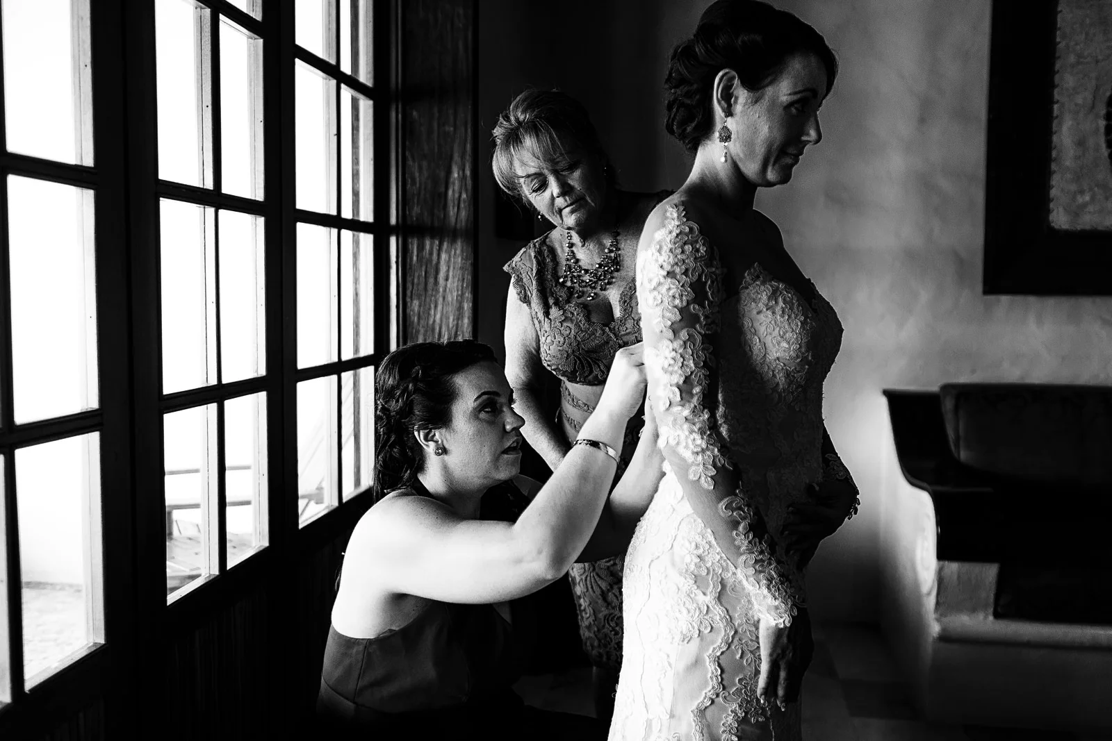 Maid of honor and mother of the bride helping the bride to get into the wedding dress
