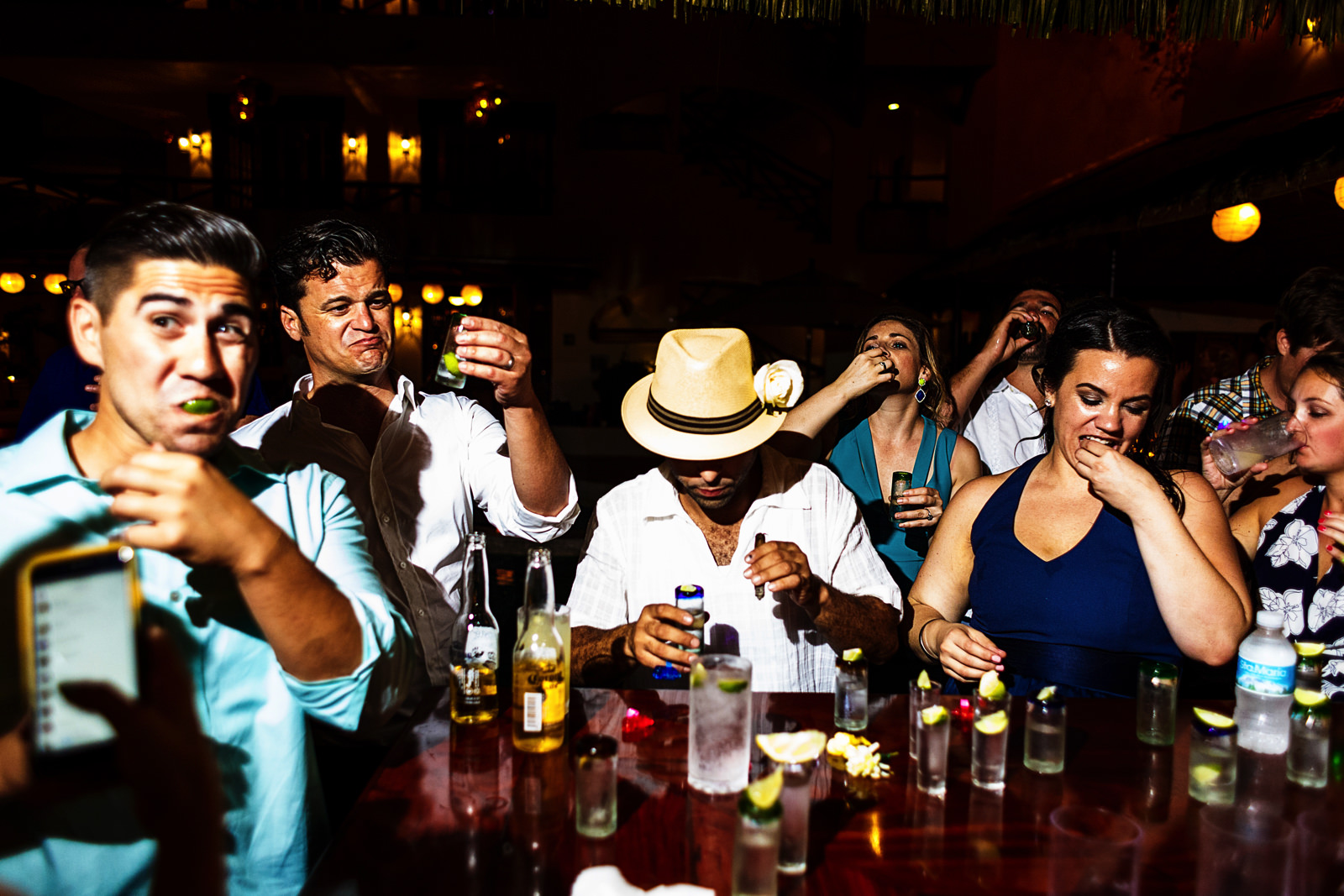 Several wedding guests having a tequila shot at the bar with the groom