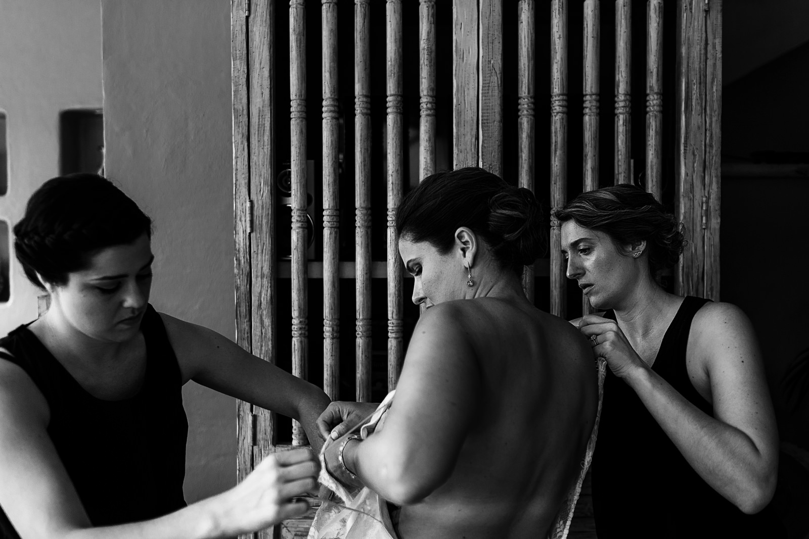 The bride is being helped by two of her girl friends to get her wedding dress on