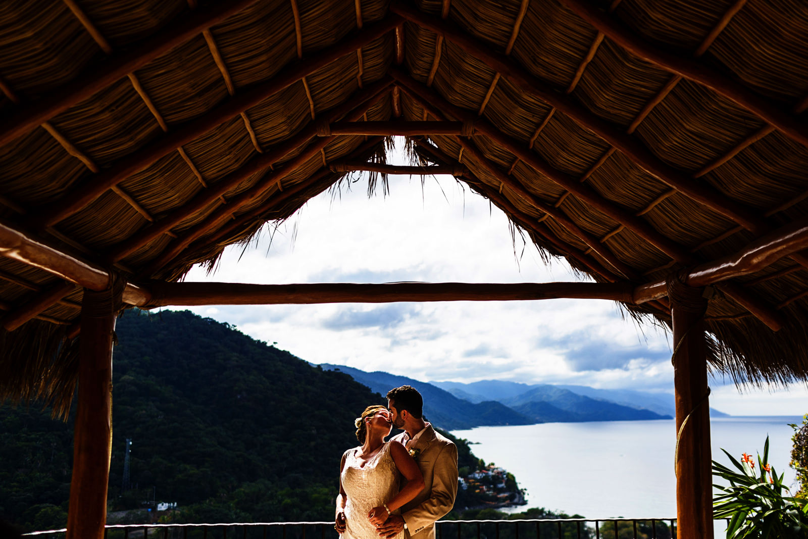A kiss of the groom and bride under a palapa roof on the terrace of a villa in Mismaloya