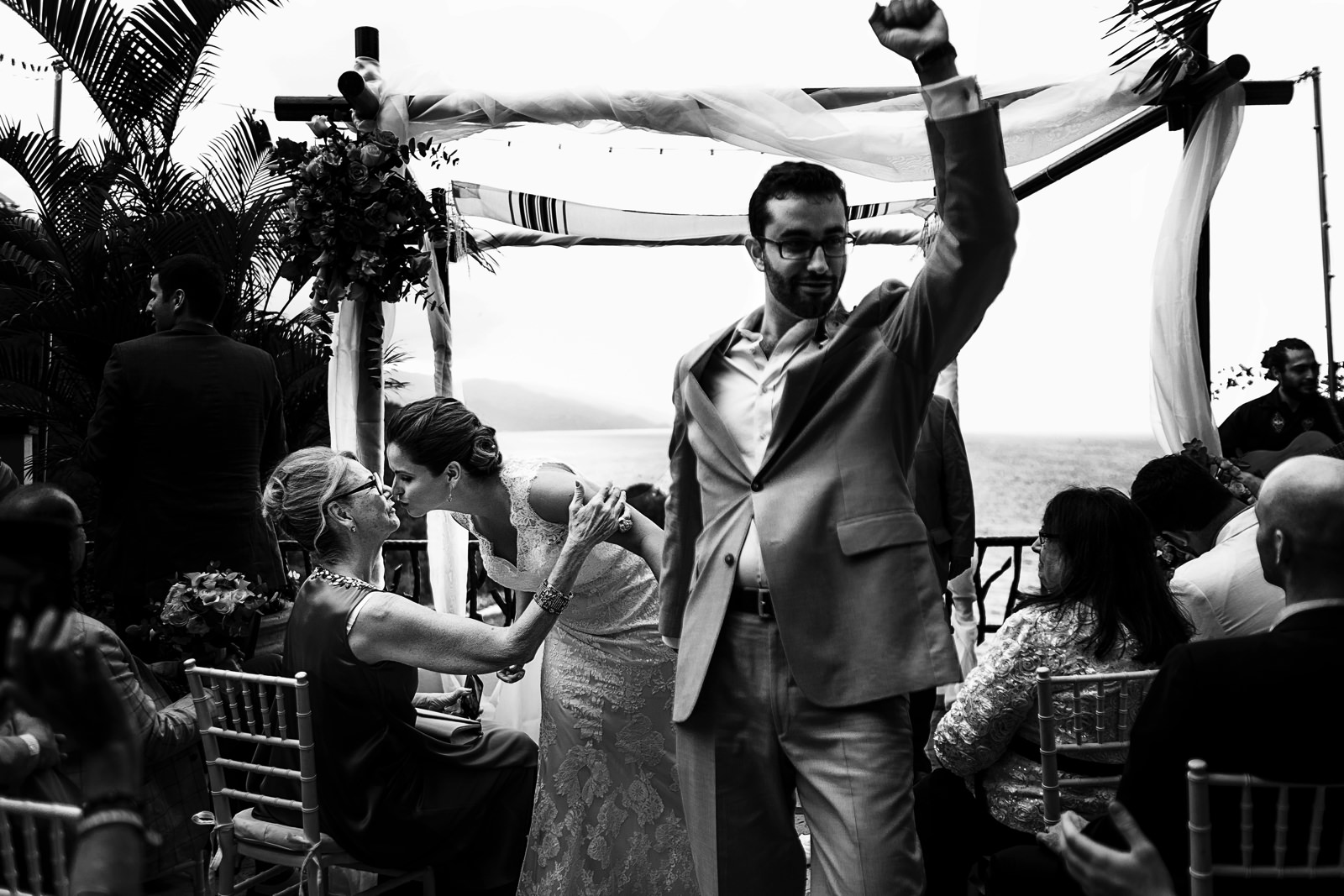 Couple walking out the ceremony, the groom raises his hand and the bride is kissing her mother