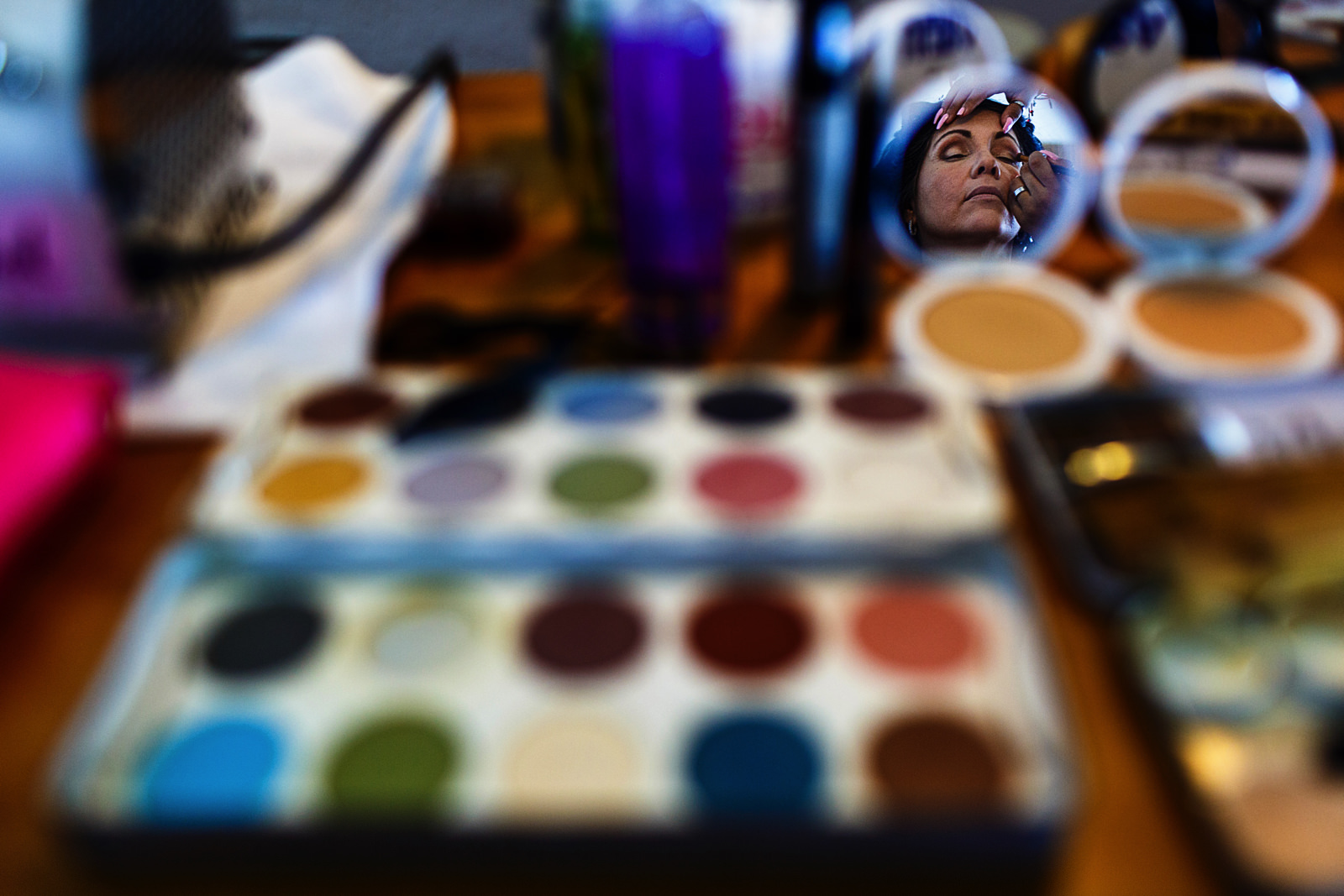 Set of make-up is laying un a table, on a mirror we see the bride's aunt's face