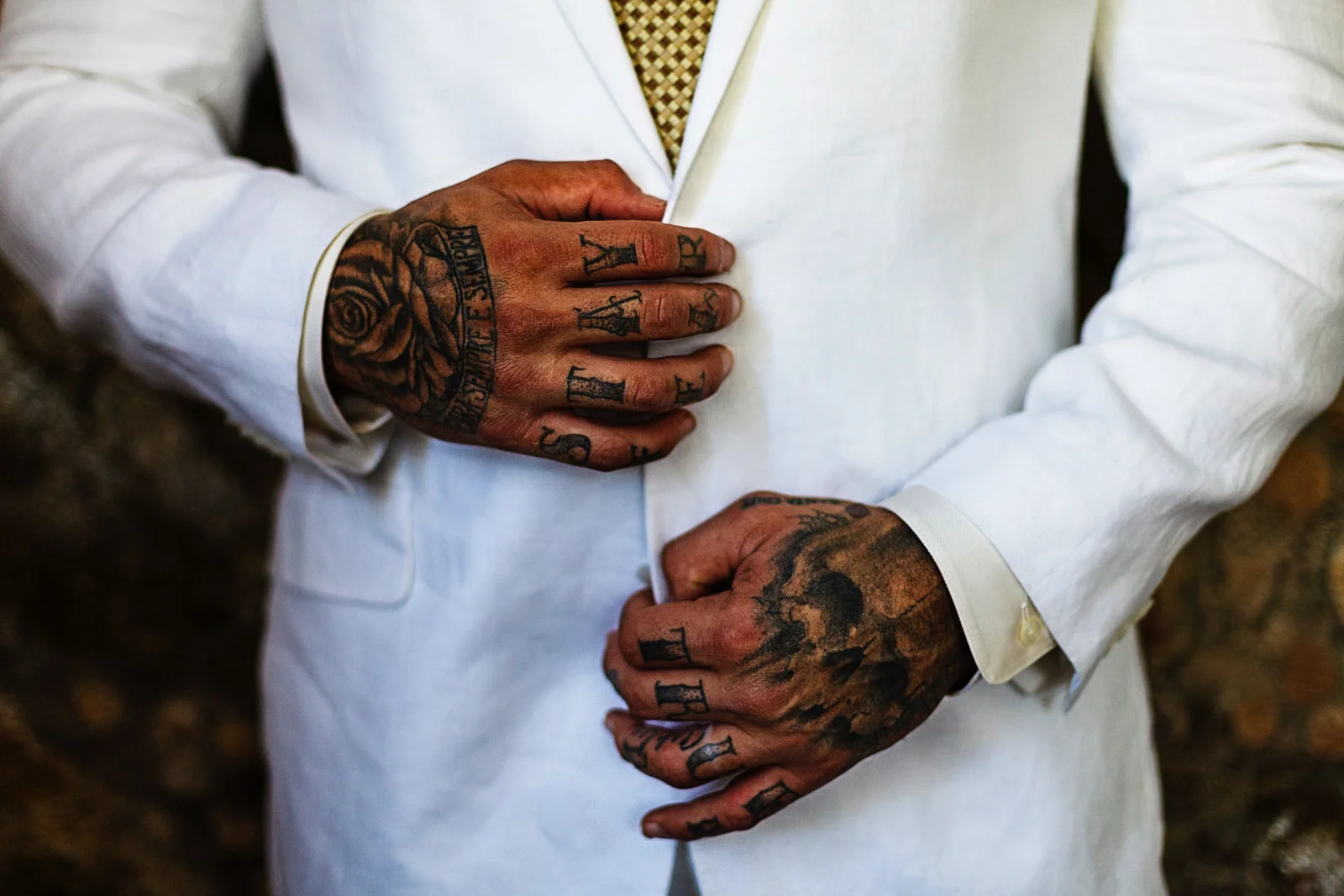 The tattooed hands of the groom are holding his suit's coat