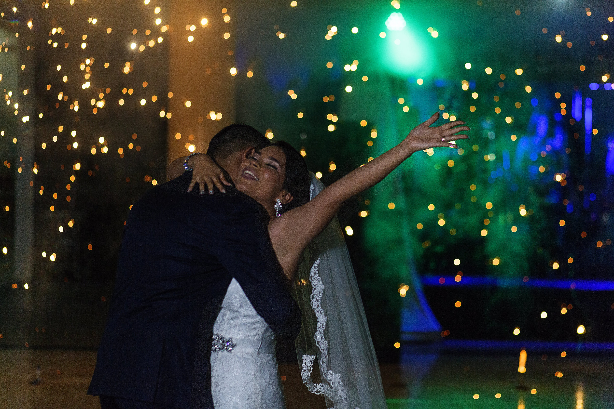 Novia sonríe y levanta su mano durante su primer baile como pareja casada, al fondo vemos el ultimo rastro de los chisperos