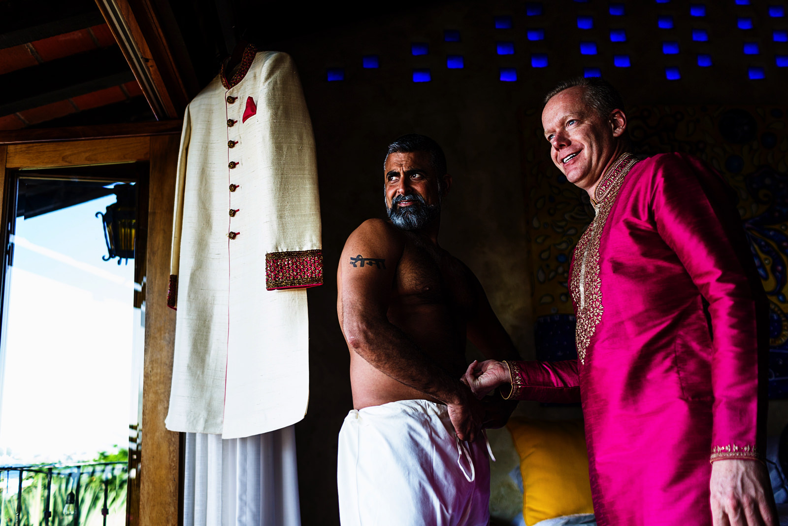 Groom and best man looking outside the window, the hindi attire is hanging on the window rack