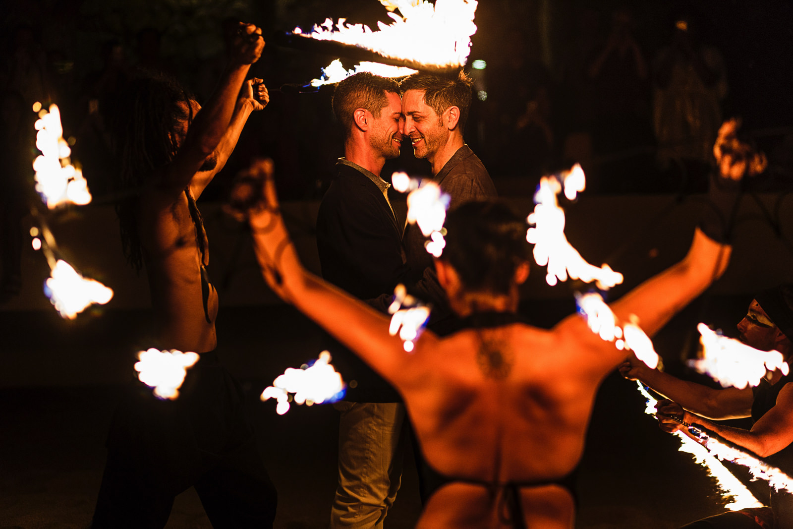 Gay couple in the middle of fire dancers as part of the entertainment during the rehearsal dinner celebration