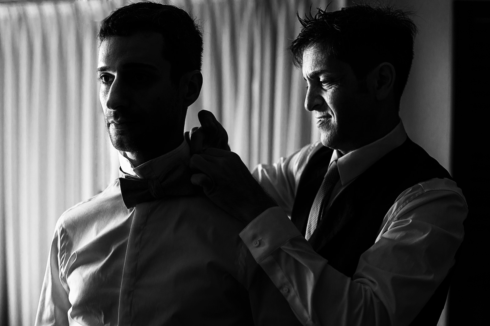 Groom helping his partner with the bow tie before the ceremony on their wedding day