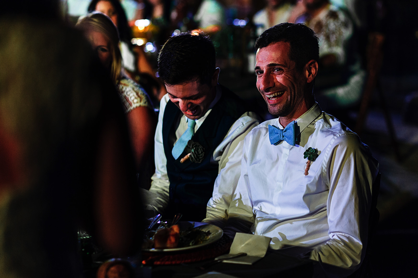 Grooms laugh as reaction while wedding guest is giving a toast speech during the dinner at Casa Karma