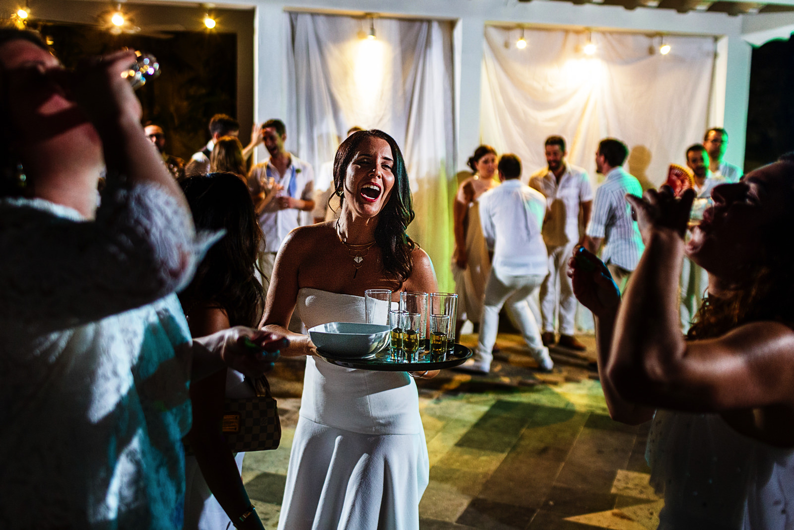 Wedding guest holds a tray of tequila shots while other two girls drink them