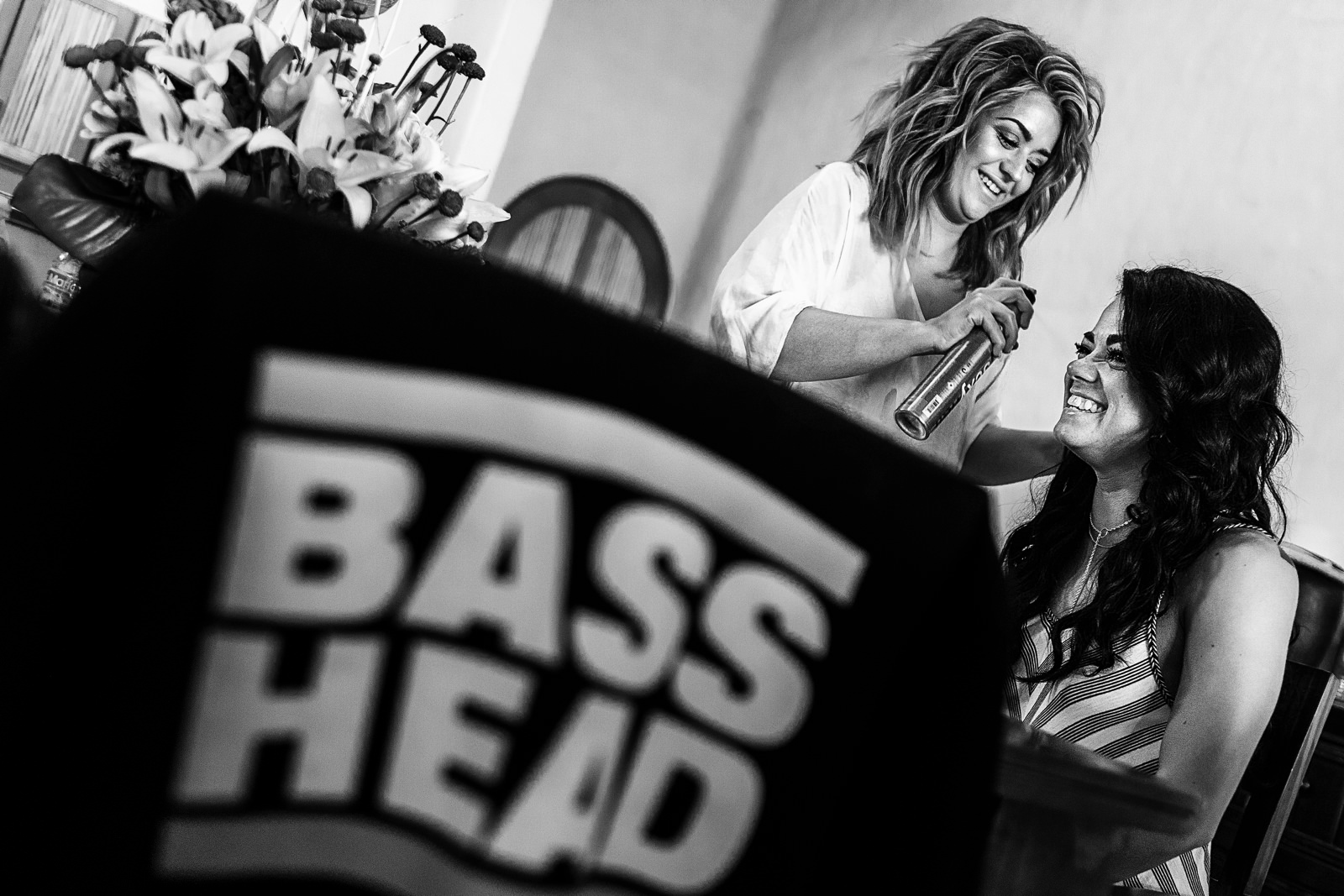 Two girls getting ready for a wedding and sharing a laugh, a BASS HEAD T-shirt is hanged over a chair in the foreground