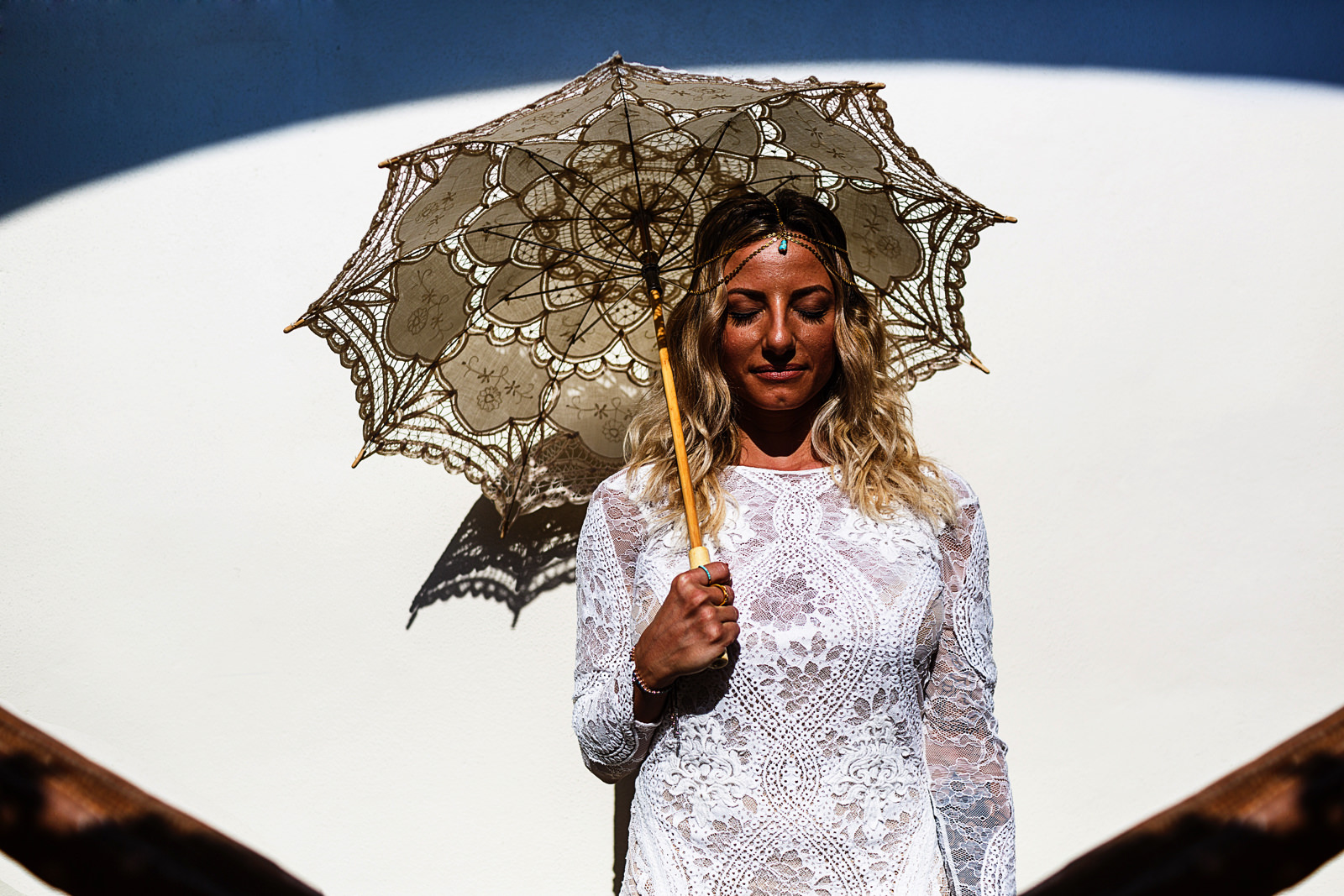 Bride portrait holding a knitted umbrella under a blue arch shadow