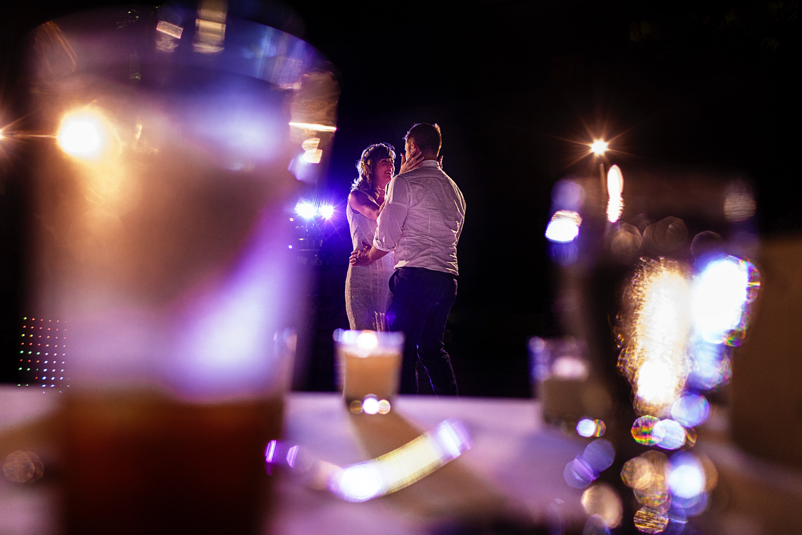 Groom and bride dance through some glasses on the table 