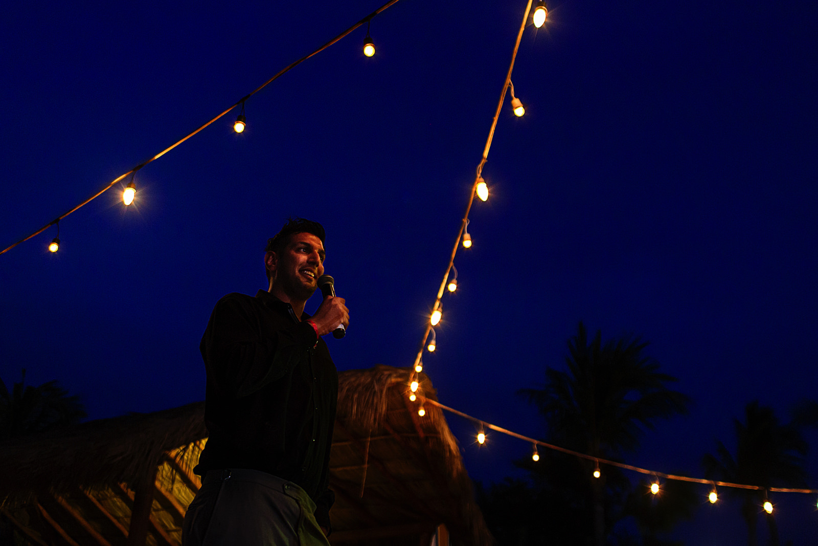 Wedding male guest giving a speech between yellow lights against the blue sky.