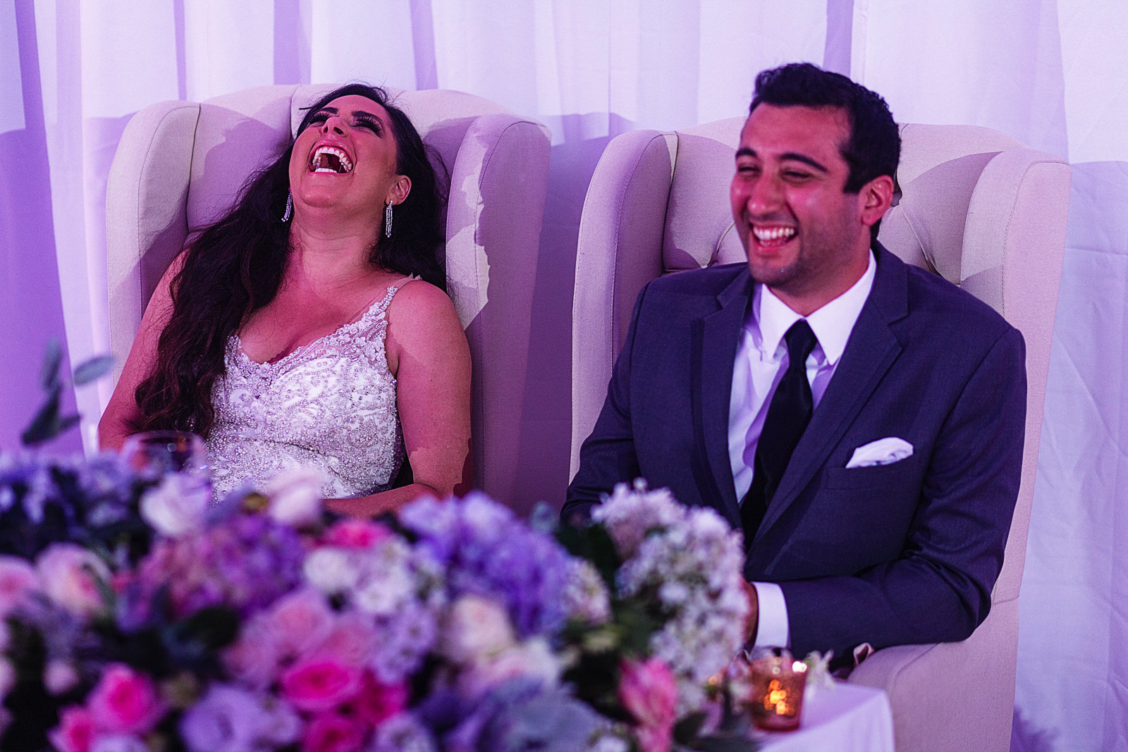 Wedding couple sitting on their table, laugh during the speeches.